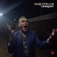 „MAKE-UP IS A LIE MORRISSEY“. Ein Mann in einem blauen Anzug schreit, seine Hände dramatisch erhoben; im Hintergrund ein Kreuz.