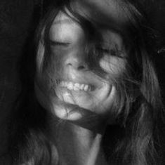 Keine Texte enthalten. Schwarz-weiß-Foto einer Frau, die lächelt, mit Haaren im Gesicht.