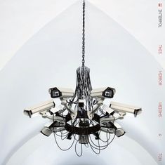 Texte: „INTERPOL THIS MIRROR WEIGHS A TON“. Eine Installation aus Überwachungskameras in Form eines Kronleuchters.