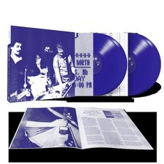 Text: "NORTH 5th. Mn DAY 9:00 PM." Zwei blaue Vinyl-Schallplatten und ein Cover mit einer Bandabbildung. Buch dazwischen.