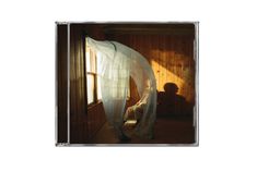 Ein Raum aus Holz, Licht strömt durch ein Fenster, ein blauer Vorhang weht, eine Person sitzt im Schatten.