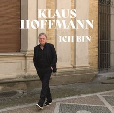 "Klaus Hoffmann, Ich bin." Ein älterer Mann in dunklem Anzug, spaziert allein auf einem Gehweg aus Kopfsteinpflaster.