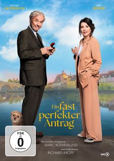 „Ein fast perfeker Antrag“. Ein Mann hält einen Ring. Eine Frau schaut überrascht. Ein kleiner Hund steht daneben.