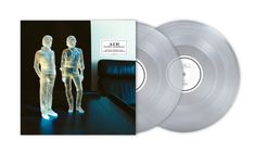 Text „AIR Pocket Symphony“. Zwei transparente Figuren, leuchten blau, stehen vor einem Sofa. Doppelte Vinylplatten sichtbar.