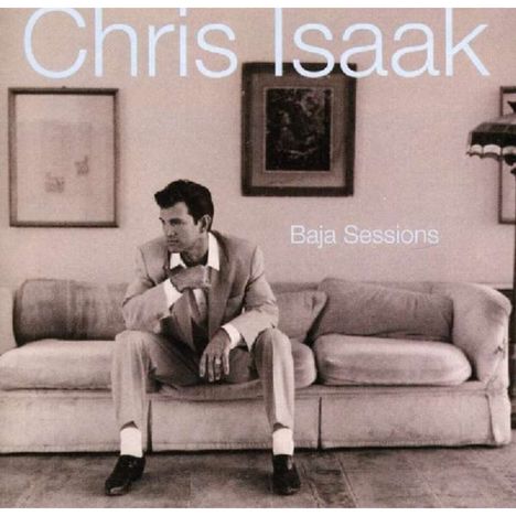 "Chris Isaak" oben, "Baja Sessions" rechts. Mann im Anzug sitzt nachdenklich auf einem Sofa, Bilder an der Wand.