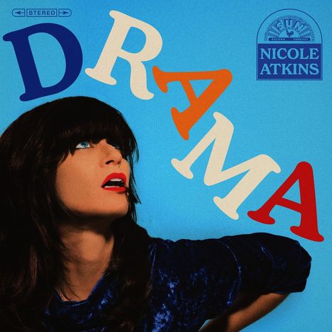 Der Text lautet "DRAMA" und "NICOLE ATKINS". Eine Frau mit dunklem Haar und rotem Lippenstift schaut nach oben.
