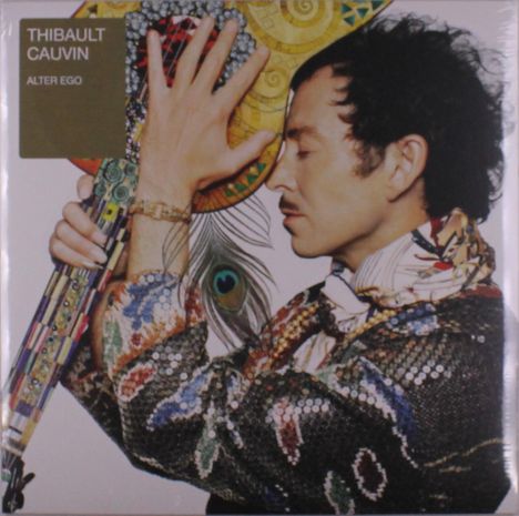 „Thibault Cauvin, Alter Ego“; ein Mann hält eine verzierte Gitarre, trägt bunte Kleidung und schaut nach rechts.