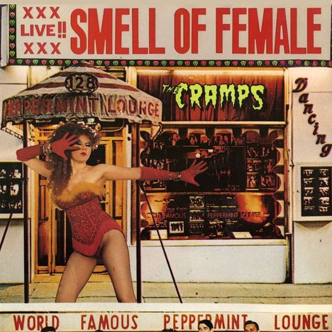 "XXX LIVE!! SMELL OF FEMALE" in großen roten Buchstaben oben. Eine Frau in rotem Outfit posiert dramatisch.