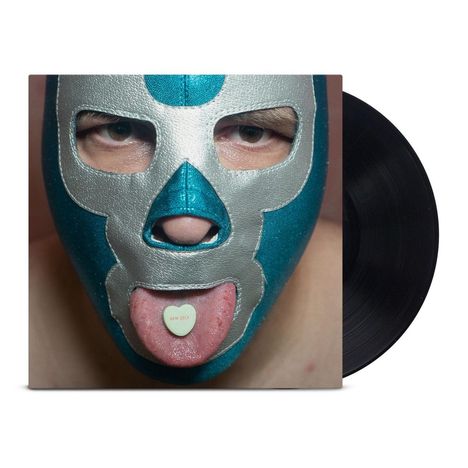 Text: "NEW SELF." Ein Mann mit Lucha-Libre-Maske, blaue und silberne Farben, hält eine Herztablette auf der Zunge.