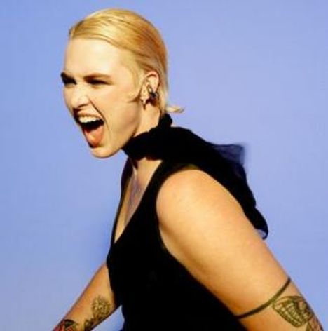 Keine Texte erkennbar. Eine Person mit blonden Haaren und Tattoos lacht oder ruft, vor blauem Hintergrund.