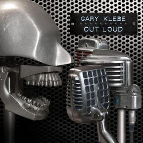 Text: "Gary Klebe Out Loud". Zwei Retro-Mikrofone und ein metallischer Schädel auf perforierter Metalloberfläche.