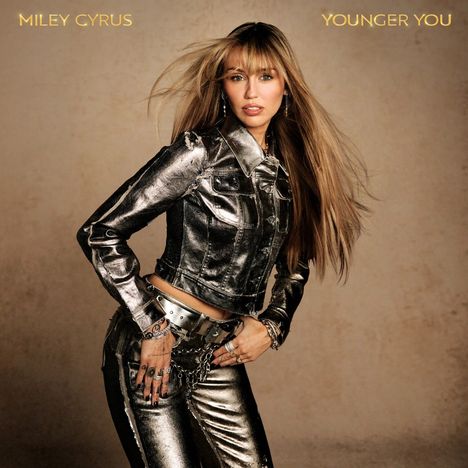 Oben links "MILEY CYRUS", rechts "YOUNGER YOU". Eine Frau in glänzender silberner Kleidung mit wehendem Haar.