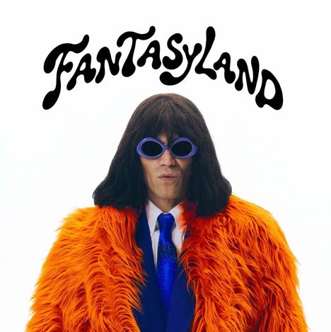 Text "FANTASYLAND" in geschwungener Schrift. Person mit dunklem Haar trägt orange Pelzmantel, blaue Brille und Krawatte.