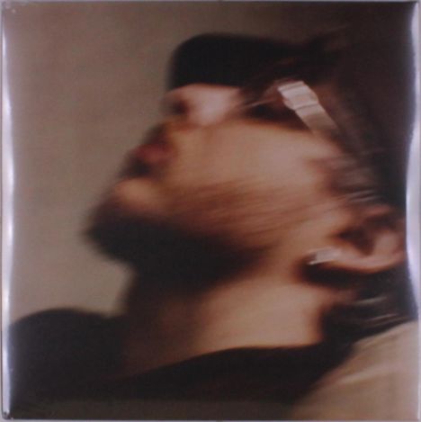 Ein unscharfes Porträt eines seitlich nach oben blickenden Mannes mit Brille und Ohrring.