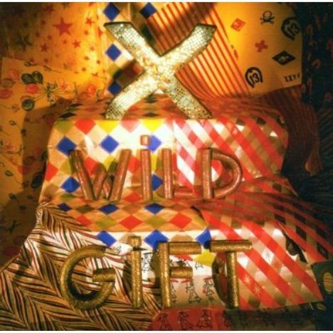 "X WILD GIFT" in goldener Schrift, umgeben von bunten, gemusterten Stoffbahnen.