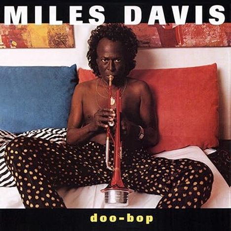 "MILES DAVIS" oben, "doo-bop" unten. Ein Mann auf einem Bett spielt Trompete, umgeben von bunten Kissen und Kunstwerken.