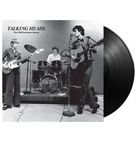 "Talking Heads: The CBS/Columbia Demos." Drei Musiker spielen Gitarre, Bass und Schlagzeug auf einer Bühne. Schwarz-Weiß-Aufnahme.