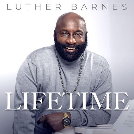 "LUTHER BARNES, LIFETIME" steht in großen Buchstaben vor einem lächelnden Mann mit Bart, grauem Pullover und Uhr.