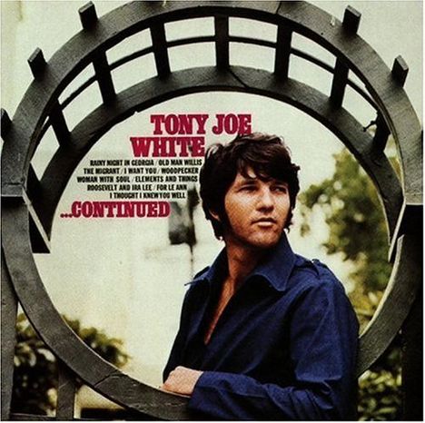 "TONY JOE WHITE ...CONTINUED." Ein Mann in dunklem Hemd steht vor einem dekorativen Metallbogen.