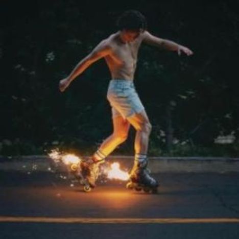Kein Text vorhanden. Ein Mann in Shorts fährt auf Rollschuhen, Funken sprühen von den Rädern auf der dunklen Straße.