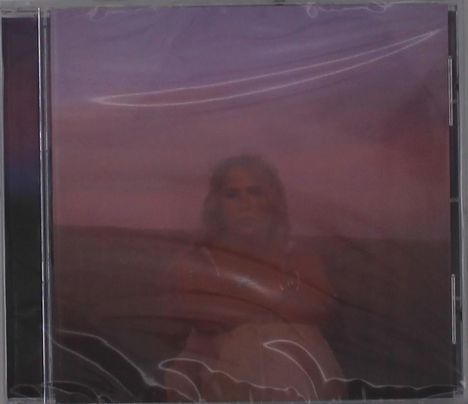 Es gibt keine erkennbaren Texte. Eine verschwommene Person sitzt vor einem rotvioletten Himmel, in Plastikfolie eingepackt.