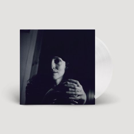 Ein Schwarz-Weiß-Foto zeigt eine Person mit nachdenklichem Ausdruck, die Hände gefaltet. Eine klare Schallplatte sichtbar.
