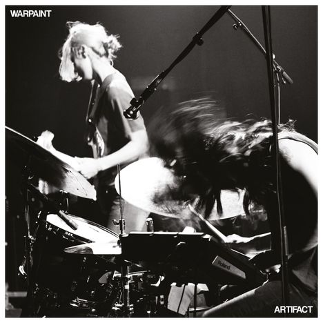 Oben links „WARPAINT“, unten rechts „ARTIFACT“. Zwei Musikerinnen auf der Bühne. Eine spielt Schlagzeug. Schwarz-weiß.