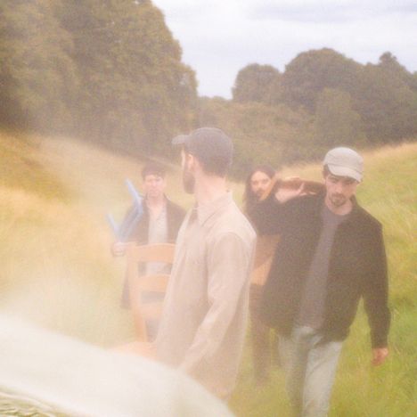 Vier Personen tragen Stühle über ein nebliges Feld; weiche, verschwommene Farbgebung.