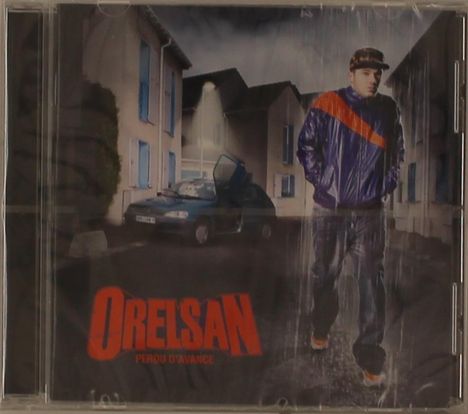 "Orelsan Perdu d'Avance" in roten Buchstaben im Vordergrund. Person in Regenmantel, Auto mit geöffneter Tür bei Nacht.