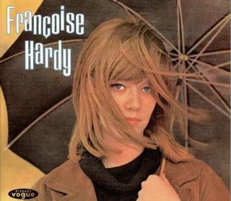 Françoise Hardy. Eine Frau mit langem Haar hält einen Regenschirm, trägt einen Mantel, schaut nachdenklich.