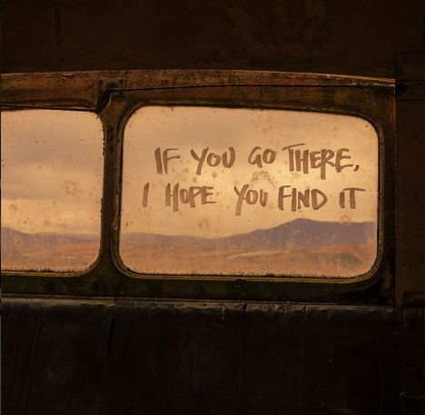 „IF YOU GO THERE, I HOPE YOU FIND IT.“ Schrift auf einer schmutzigen Fensterscheibe mit Landschaft im Hintergrund.