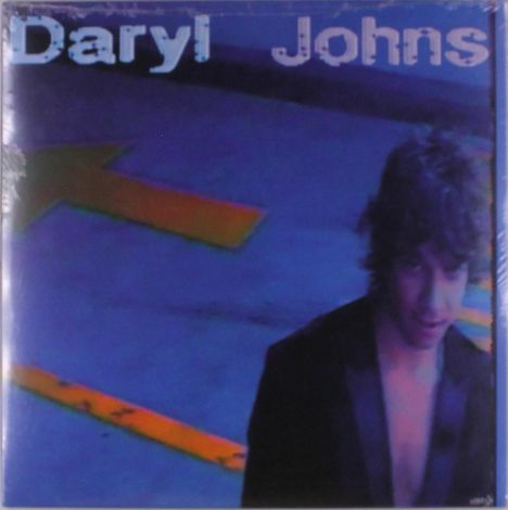 Text: "Daryl Johns". Eine Person vor blauem Hintergrund mit gelbem Pfeil, trägt ein dunkles Kleidungsstück.