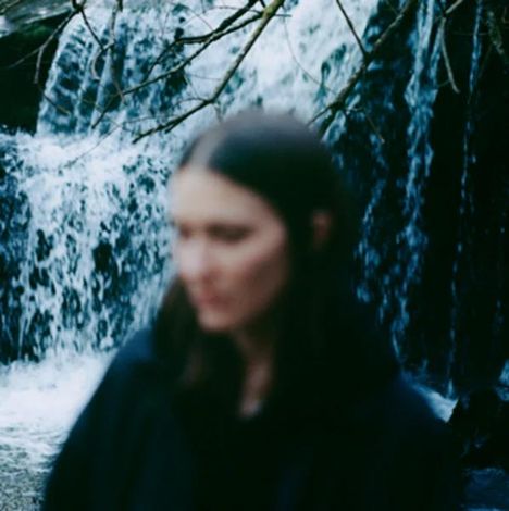 Unscharfe Person im Vordergrund, verwässerter Wasserfall und Baumzweige im Hintergrund.