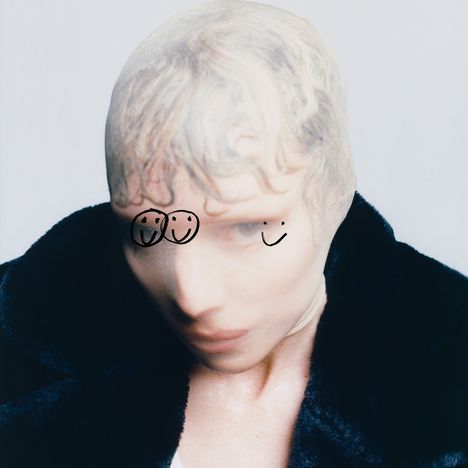 Zwei gezeichnete Smileys auf einem Gesicht mit nassen Haaren und dunklem Mantel.