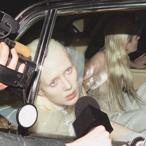 Eine Person mit blonden Haaren schaut aus einem Autofenster; Mikrofone sind darauf gerichtet.