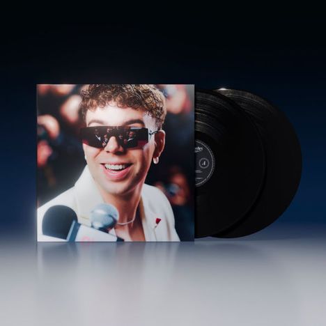 Ein lächelnder Mann mit Sonnenbrille vor Mikrofonen auf einem Plattencover, daneben zwei schwarze Vinyl-Schallplatten.