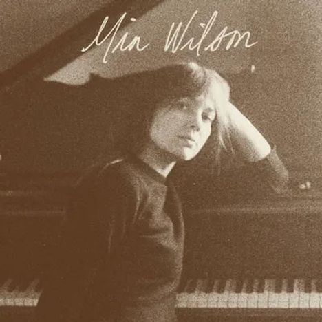 Der Text "Mia Wilson" steht oben. Eine Frau sitzt nachdenklich an einem Klavier und schaut zur Seite.