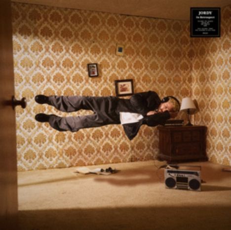 Text: "JORDY, Die Notaufnahme". Ein Mann schwebt horizontal mit Kopfhörern in einem Zimmer, Retro-Tapete im Hintergrund.