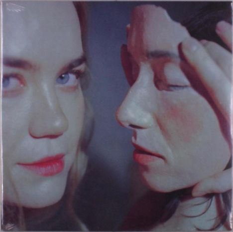 Zwei weibliche Gesichter. Die linke Person schaut direkt, die rechte hält ein Maskenfragment ans Gesicht, Augen geschlossen.