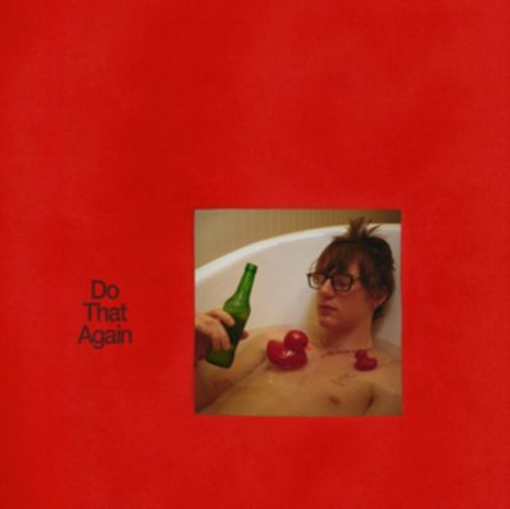 Text: „Do That Again“. Ein Mann mit Brille in der Badewanne hält eine Flasche, umgeben von roten Quietscheenten.