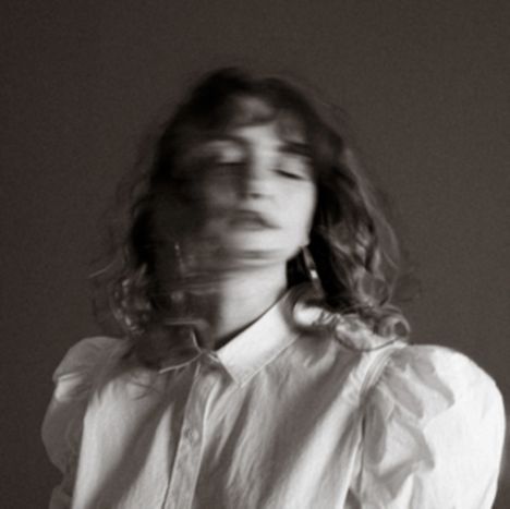 Keine Texte sichtbar. Verschwommenes, monochromes Bild einer Frau mit lockigem Haar in weißem Hemd.