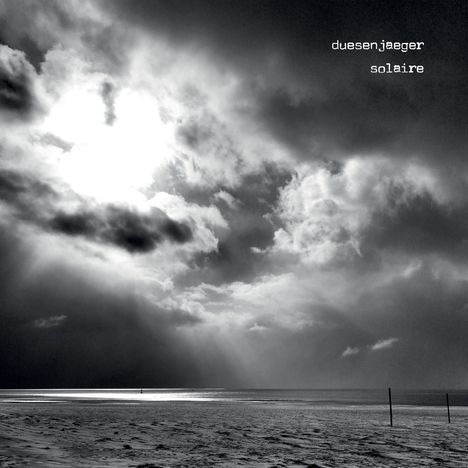 Texte: duesenjaeger, solaire. Lichtstrahlen durch Wolken über einem ruhigen Meer an einem sandigen Strand.