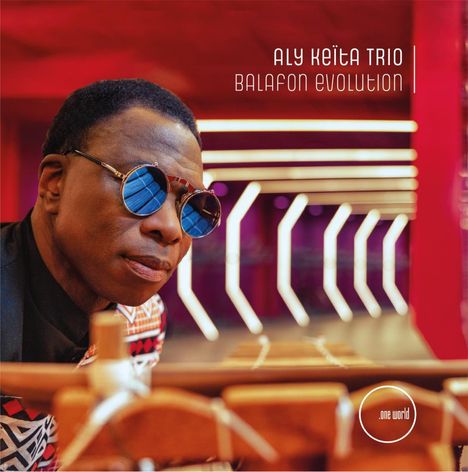 "Aly Keïta Trio, Balafon Evolution." Ein Mann mit Sonnenbrille, im Hintergrund moderne, geometrische Beleuchtung.