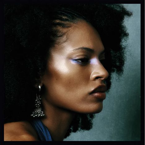 Ich kann keinen Text im Bild erkennen. Es zeigt eine Frau im Profil mit schillerndem Make-up und lockigem Haar.