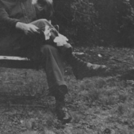 Ein Mensch sitzt auf einer Bank in einem Garten, hält eine Blume und streichelt einen Hund. Alles ist in Schwarz-Weiß gehalten.