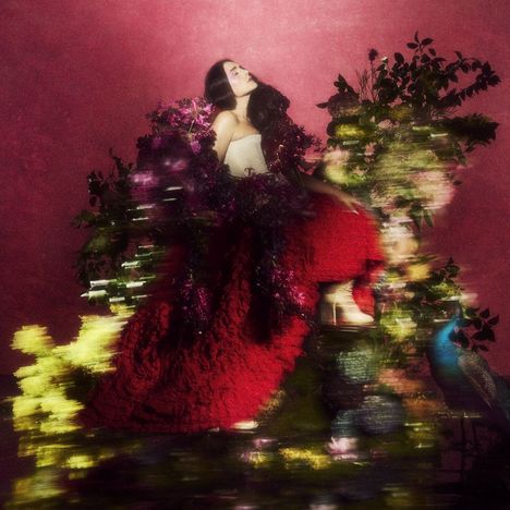 Keine Texte vorhanden. Eine Frau in einem roten Kleid sitzt träumerisch inmitten von Blumen und Pflanzen vor rosafarbenem Hintergrund.