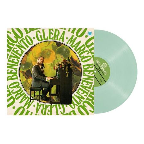 "Marco Benevento" und "GLERA" in großen, grünen Buchstaben. Ein Mann am Klavier, Blumen darauf, beige und grüne Vinyl-Schallplatte.