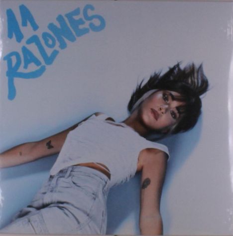 Der Text "11 RAZONES" ist in blauer Schrift zu sehen. Eine Frau liegt, der Blick nach oben gerichtet, in hellem Oberteil und Jeans.