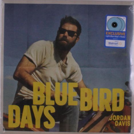 Text: „BLUE BIRD DAYS“ und „JORDAN DAVIS“. Ein Mann mit Sonnenbrille fährt Motorrad. Ein Aufkleber weist auf eine exklusive Ausgabe hin.