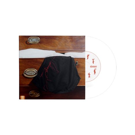 Ein weißer Kreis mit "simmer" in Rot und Figuren; schwarzer Stoff auf brauner Holzkommode.